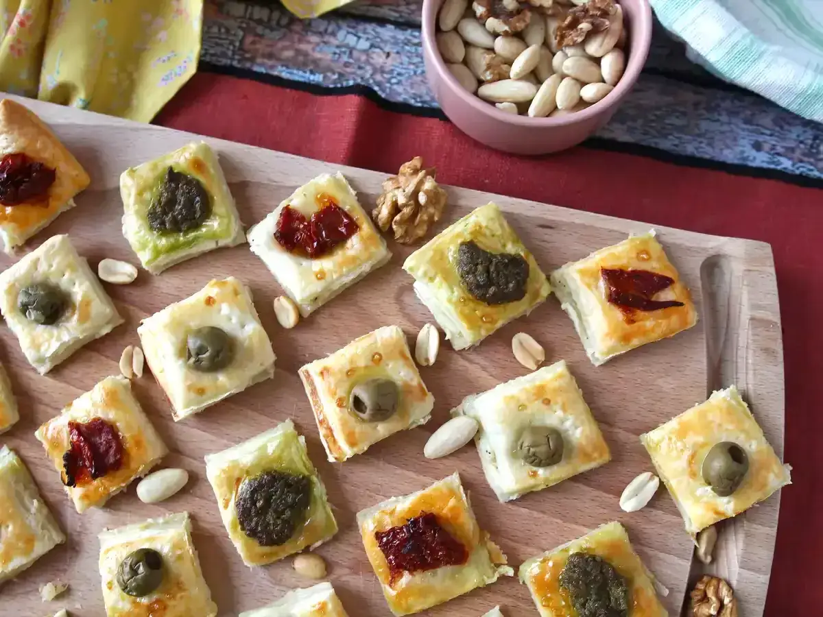 Assortiment de petits fours sal&eacute;s en p&acirc;te feuillet&eacute;e, garnis de pesto, d'olives ou de tomates s&eacute;ch&eacute;es.