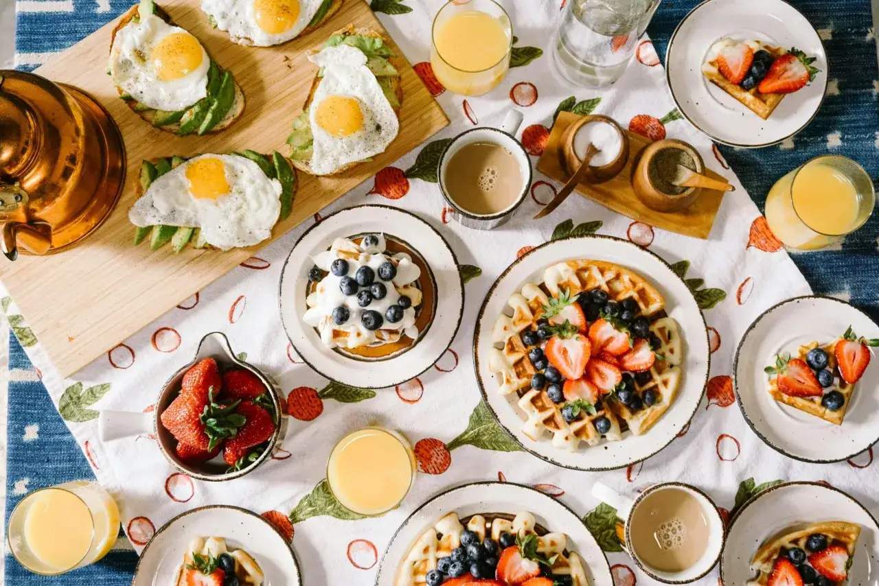 Un petit déjeuner continental ou américain avec toasts à l'avocat et œufs, gaufres aux fruits rouges et myrtilles, jus d'orange et café.