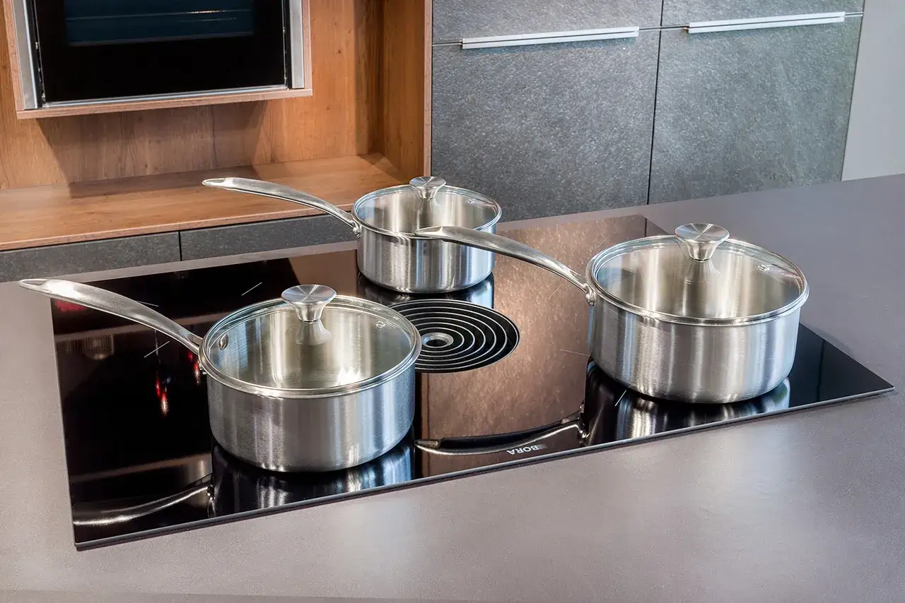 Trois casseroles en inox avec couvercles en verre sont prêtes sur une plaque à induction. Ces casseroles qui vont au four sont parfaites pour toutes vos préparations culinaires.