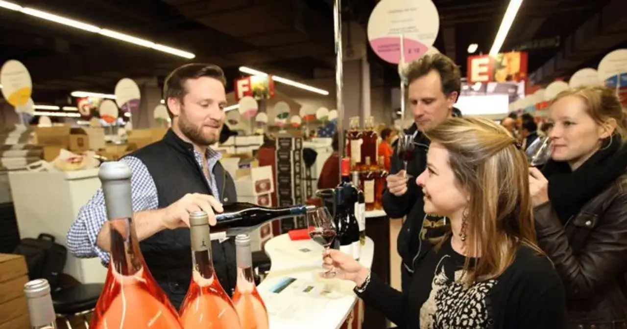 Un homme verse du vin à une femme lors d'une dégustation. Des bouteilles de rosé sont posées sur le comptoir, participant aux jeux du goût.