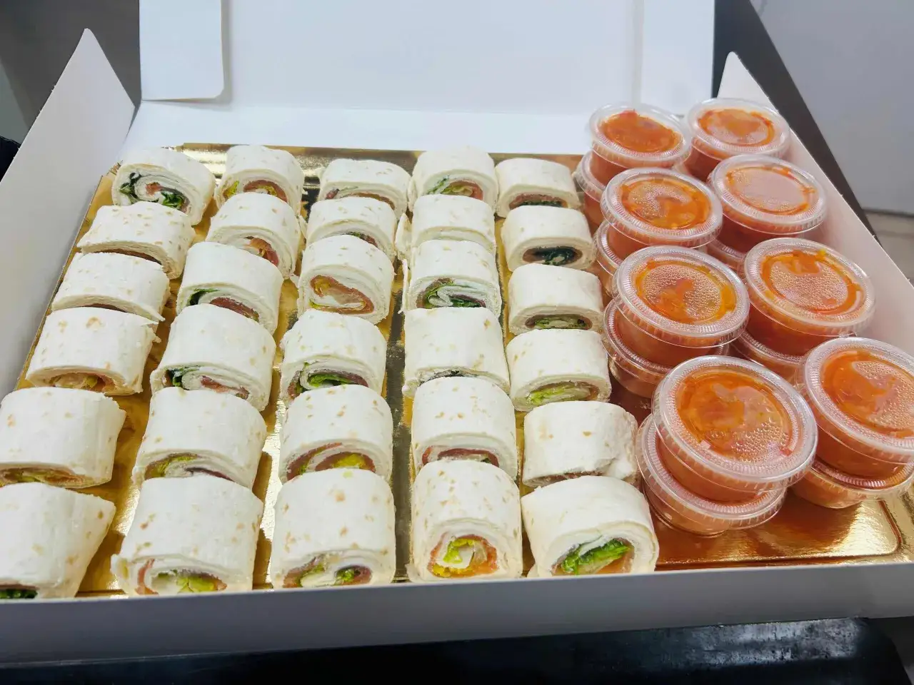 Plateau de petits fours apéro : roulés de tortillas garnis de saumon fumé, fromage frais et salade, accompagnés de sauces.