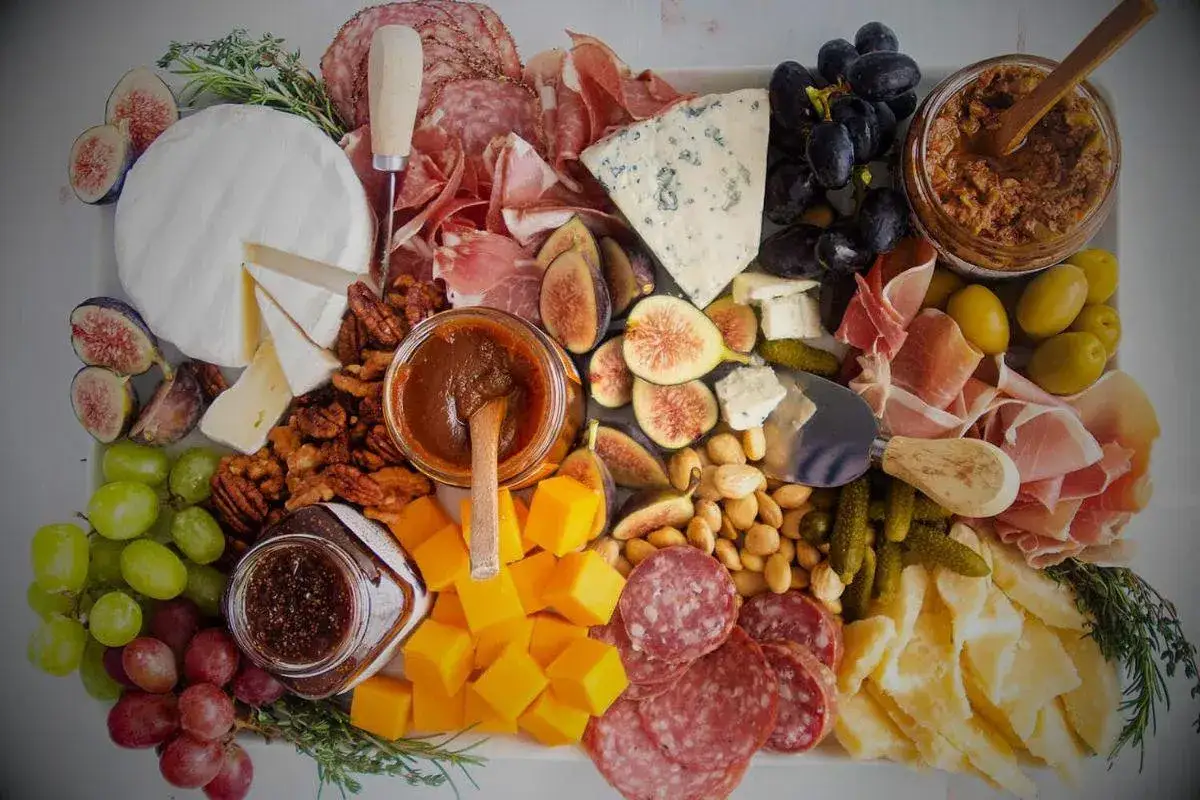Un plateau de charcuterie et fromages varié : jambon, saucisson, brie, bleu, figues, raisins, olives, noix et confitures. Un buffet idéal pour un apéritif gourmand.