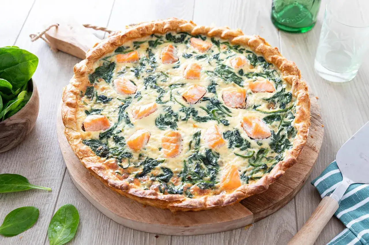 Une délicieuse quiche saumon épinard frais, garnie de morceaux de saumon rose et d'épinards verts, sur une pâte dorée.