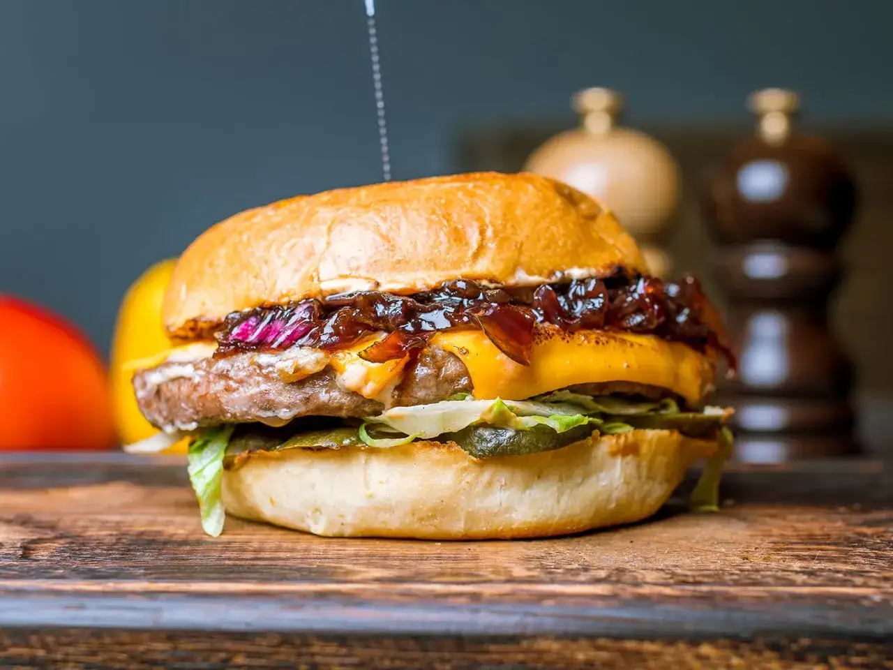 Un succulent steak burger avec fromage fondu, oignons caramélisés et cornichons, sur une planche en bois.