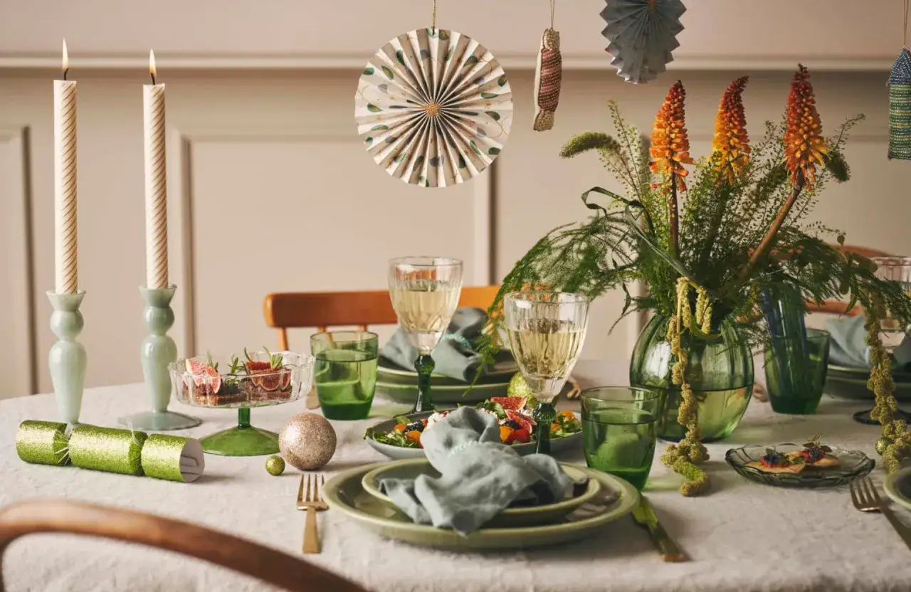 Table dressée pour une fête familiale : bougies, fleurs, vaisselle verte et décorations festives.