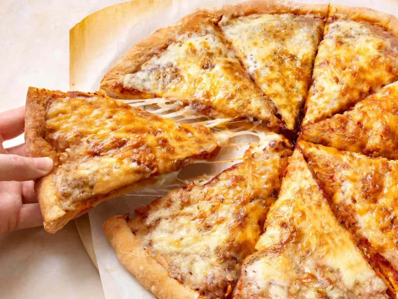 Une main soulève une part de pizza dégoulinante de fromage, parfaite après une cuisson idéale dans un four à pizza.