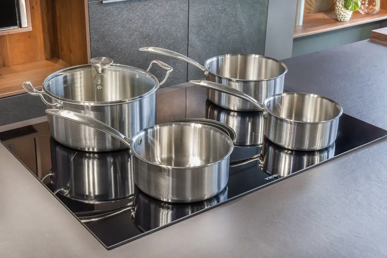 Ensemble de casseroles et poêles en acier inox 18/10, brillantes et modernes, posées sur une plaque de cuisson vitrocéramique noire.