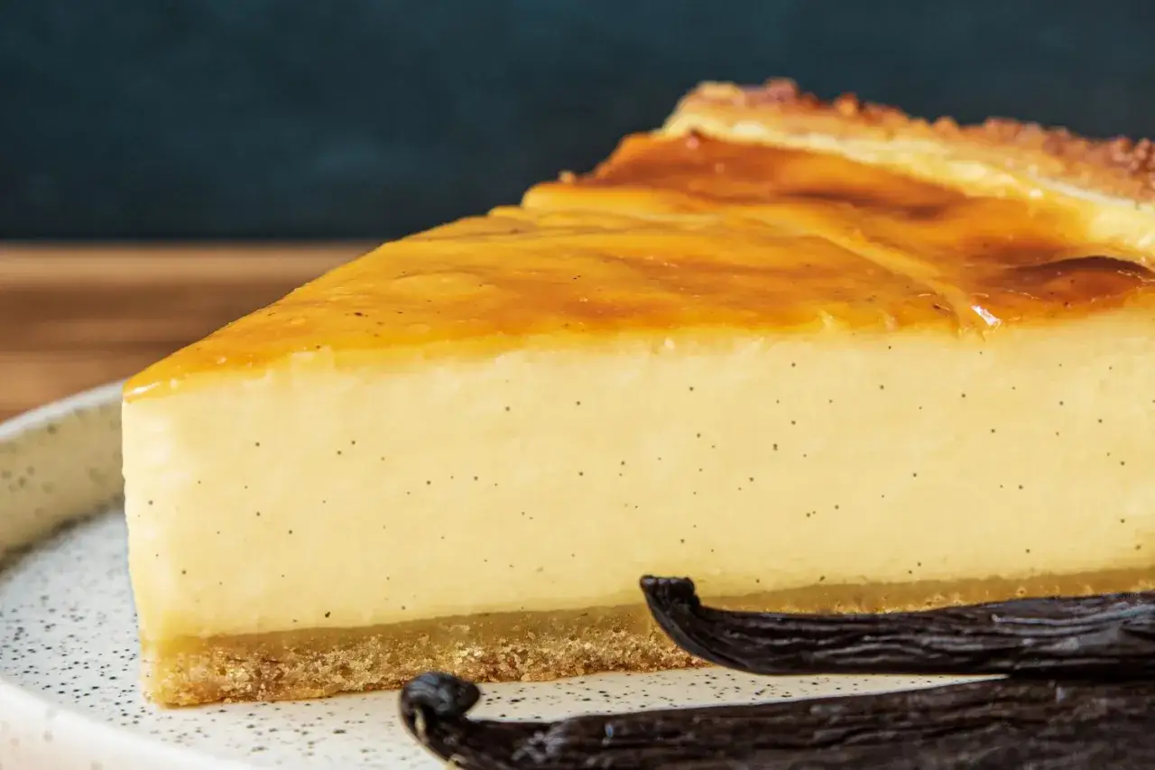 Une part de flan onctueux à la vanille, signature de Cyril Lignac, sur une assiette, avec des gousses de vanille.