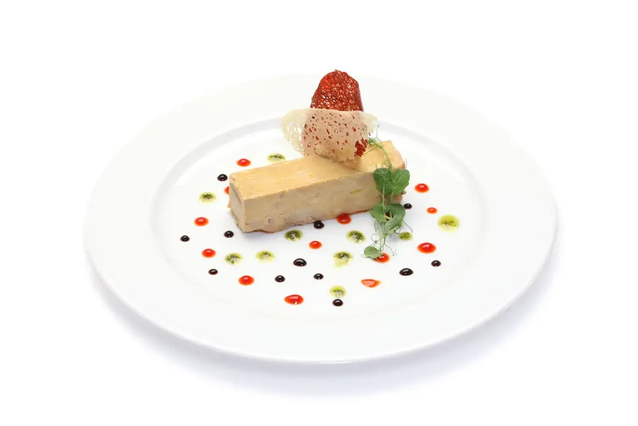 Assiette de foie gras, une présentation raffinée avec des touches de sauce rouge et verte, un biscuit croustillant et une feuille de pois.