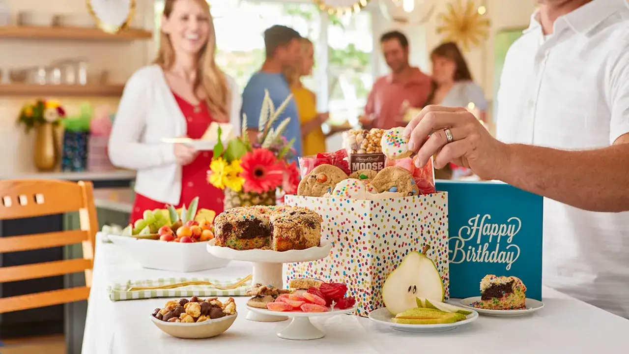 Un buffet d'anniversaire ado 18 ans festif avec gâteau, cookies, fruits et bonbons. Une main attrape un cookie décoré.