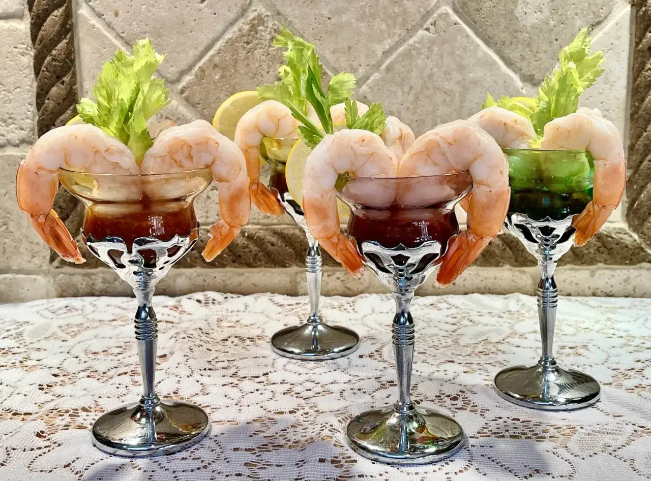 Quatre coupes élégantes présentent des crevettes roses servies avec une sauce rouge et une branche de céleri. Un cocktail sans citron, parfait pour l'apéritif.