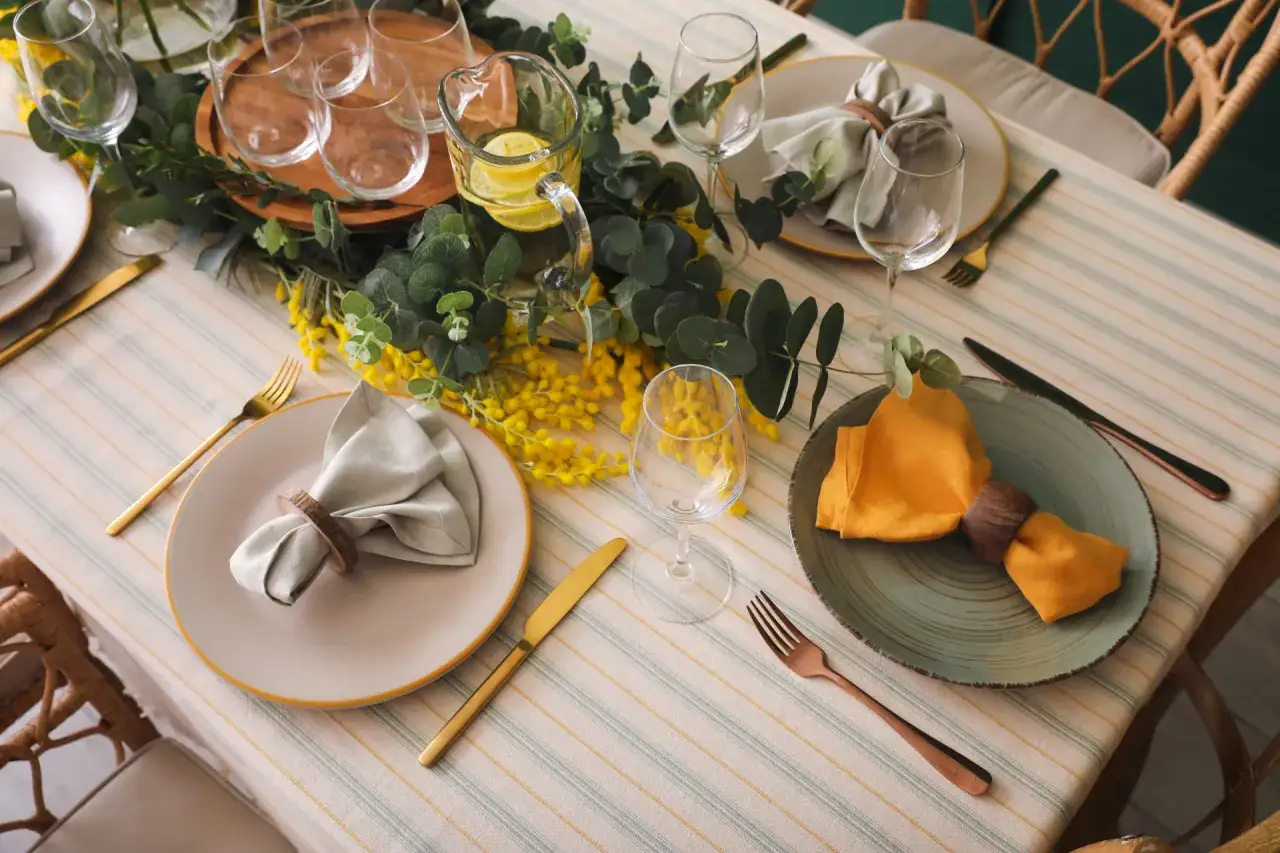 Une table joliment dress&eacute;e pour un d&eacute;jeuner d'anniversaire, avec des fleurs jaunes, de la verdure et des assiettes &eacute;l&eacute;gantes.