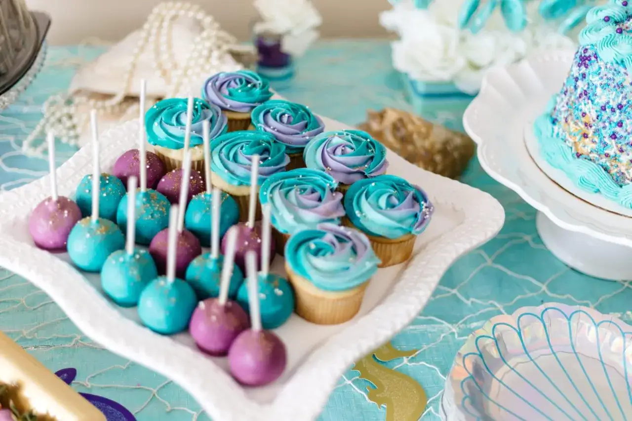 Un délicieux repas baby shower avec des cake pops violets et bleus, des cupcakes aux couleurs dégradées et un gâteau scintillant.