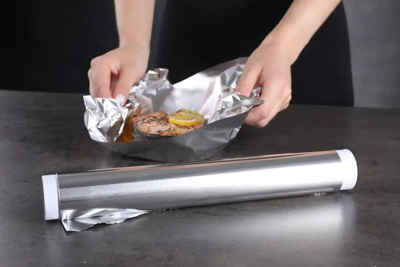 Pr&eacute;paration d'un saumon au citron dans du alu four. Les mains ajustent le papier d'aluminium autour du poisson.