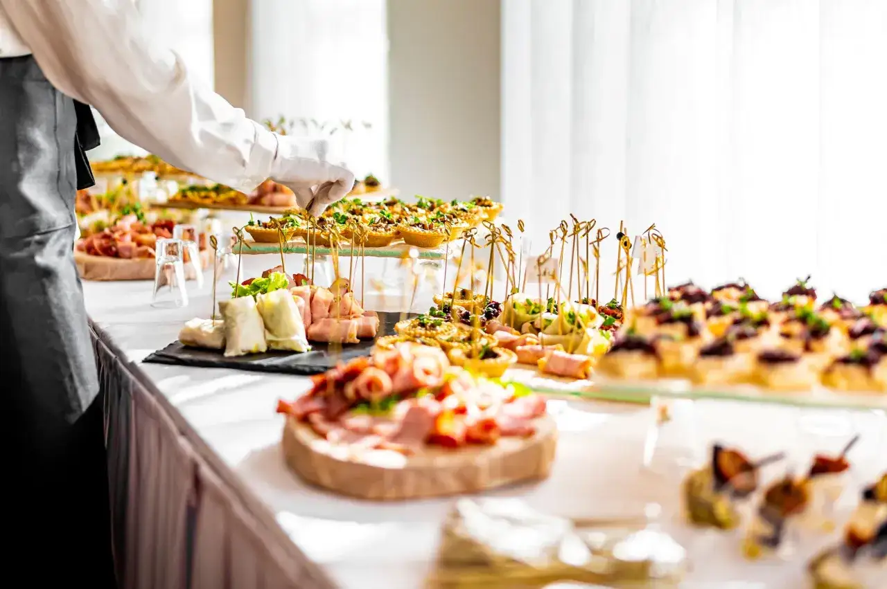 Un serveur en gants blancs ajuste des amuse-bouches sur un buffet. Un délicieux repas d'anniversaire est prêt à être dégusté.