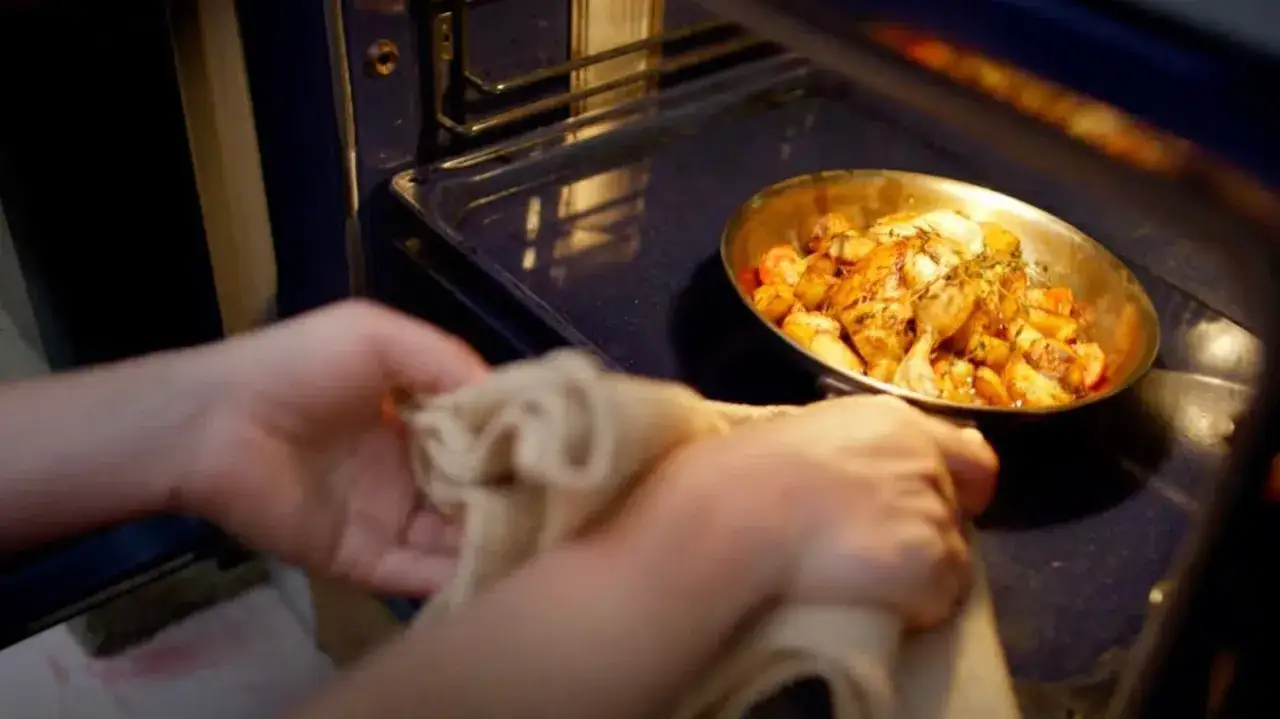 Une po&ecirc;le contenant un poulet r&ocirc;ti et des pommes de terre est retir&eacute;e du four. Oui, on peut mettre une po&ecirc;le au four si elle est adapt&eacute;e.