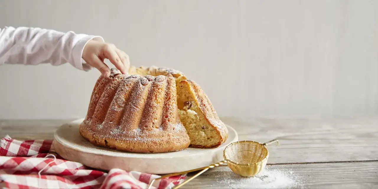 Une main d'enfant effleure un savoureux g&acirc;teau en forme de couronne, une d&eacute;licieuse entr&eacute;e alsacienne saupoudr&eacute;e de sucre glace.