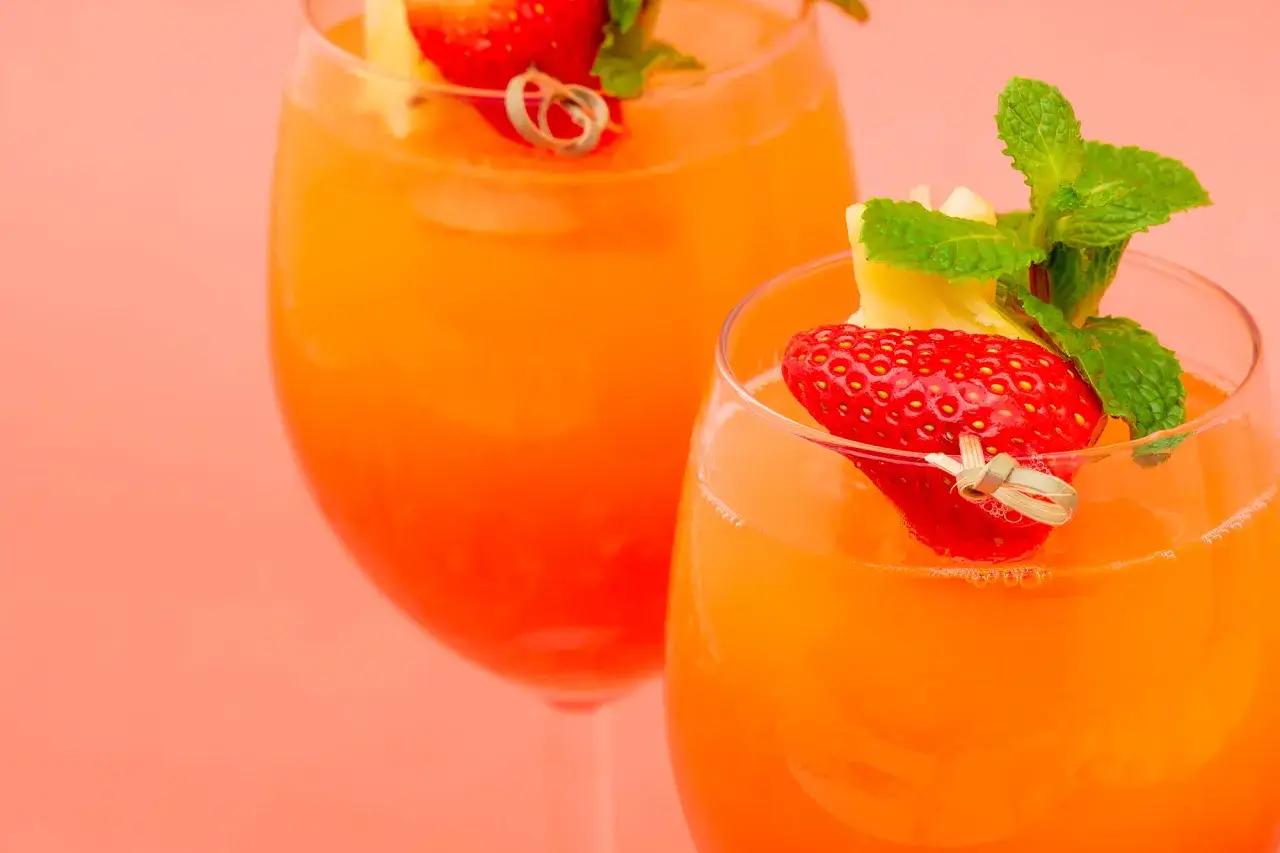 Deux verres de cocktail sans alcool anniversaire, décorés de fraises, d'ananas et de menthe, sur fond rose corail.