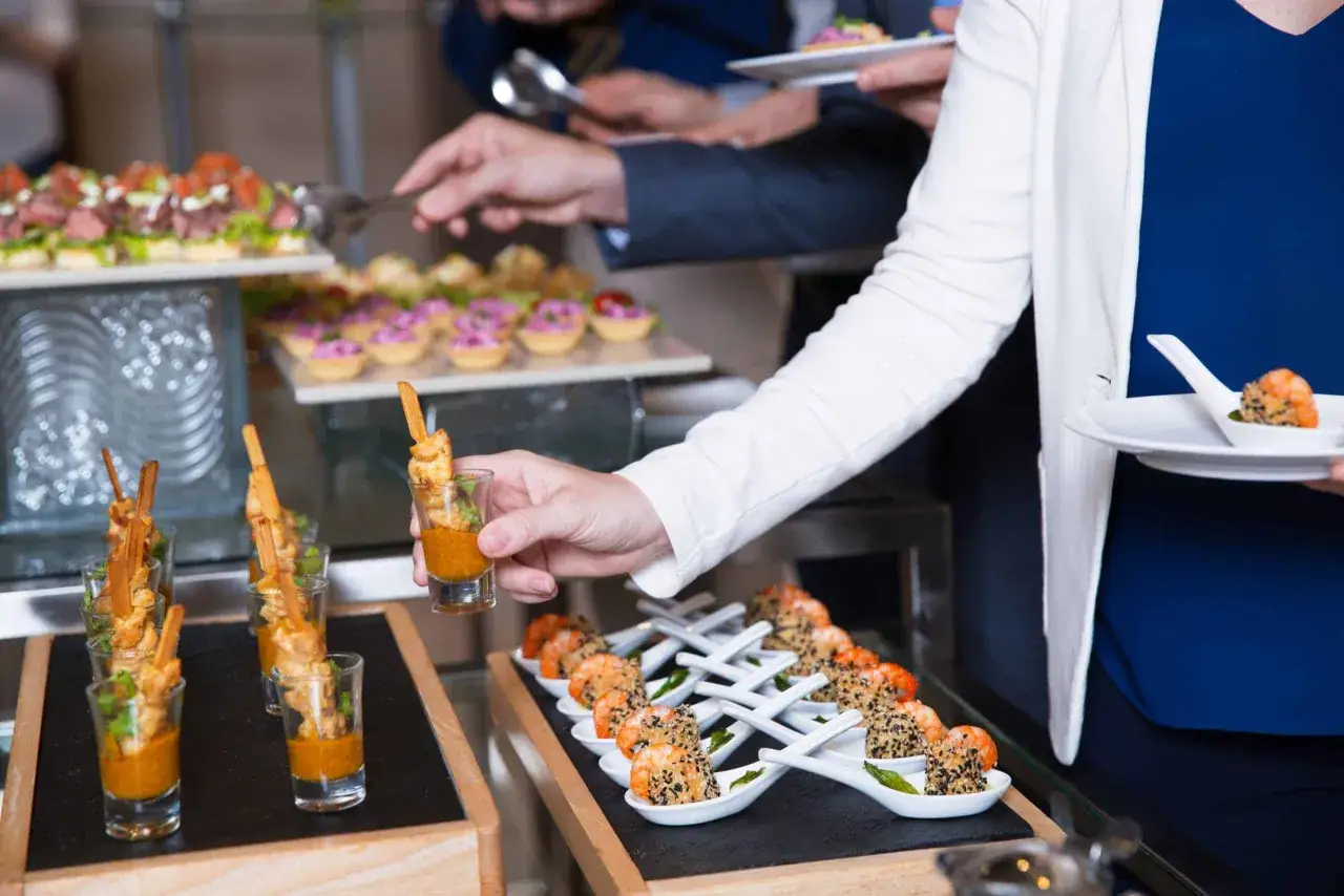 Des convives se servent pour faire un buffet froid. Petites bouch&eacute;es vari&eacute;es, crevettes et brochettes sont pr&eacute;sent&eacute;es.