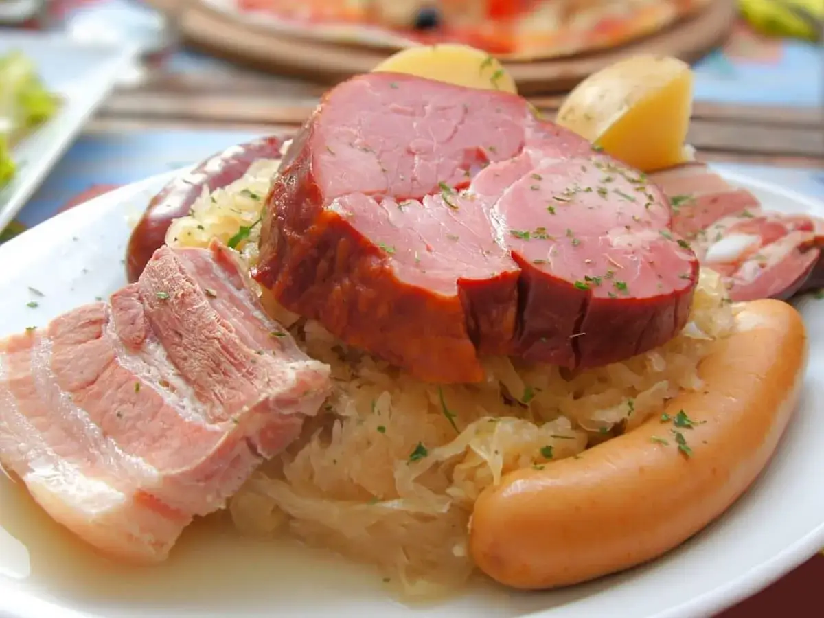 Une assiette copieuse d'une entr&eacute;e alsacienne : jambonneau, saucisses, lard et choucroute garnie, le tout saupoudr&eacute; d'herbes.