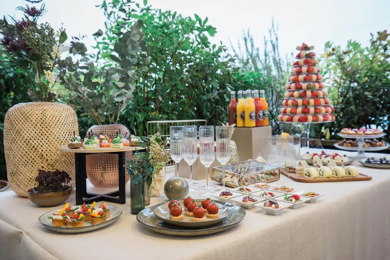 Un magnifique buffet d&eacute;jeuner en ext&eacute;rieur, avec des verrines, des fruits, des jus et une pyramide de macarons et fraises.