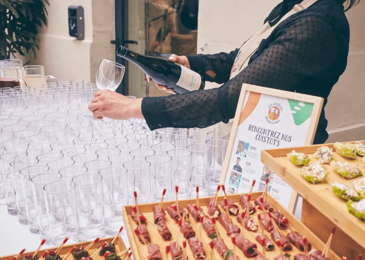 Une personne verse du vin pour un ap&eacute;ro dinatoire, avec des verrines et des petits fours sur la table.