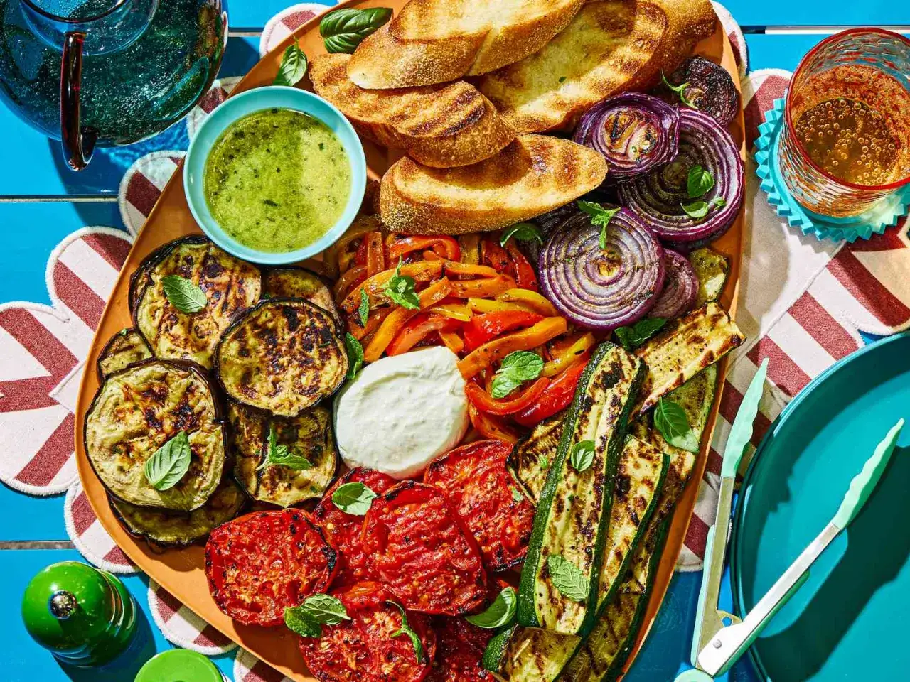 Un grand plat de légumes grillés, tomates, courgettes, aubergines, poivrons, oignons rouges, pain grillé et sauce verte. Un plat méditerranéen parfait pour partager.