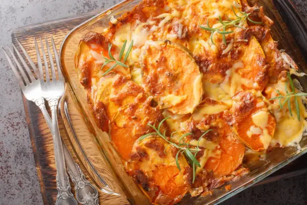 Gratin de patates douces au fromage, prêt pour un repas d'anniversaire. Deux fourchettes argentées sont posées sur le côté.