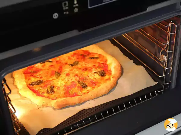 Une pizza dorée cuit dans un four, sa croûte gonflée et son fromage fondant témoignent de la parfaite fonction pizza four.