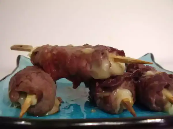 Brochettes de boeuf roulées autour de fromage fondant, servies sur une assiette bleue.