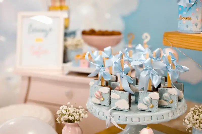 Garniture de table pour baby shower avec des chocolats décorés de montgolfières bleues et de nuages.